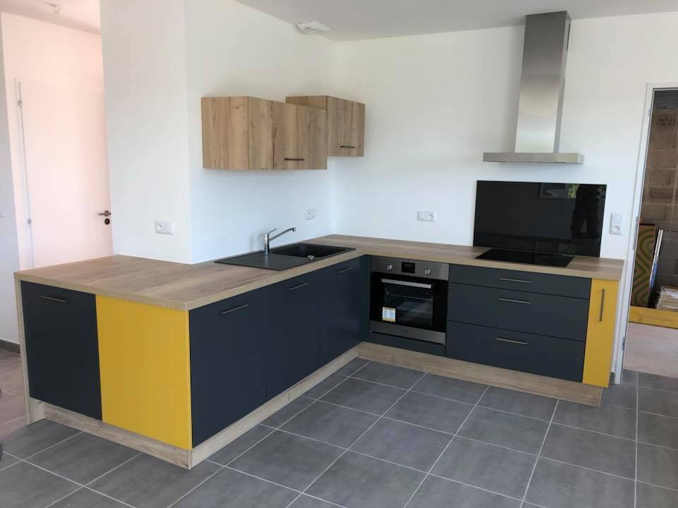 Création d'une cuisine en S bleu foncé, jaune et bois clair avec hotte inox murale à Montpellier