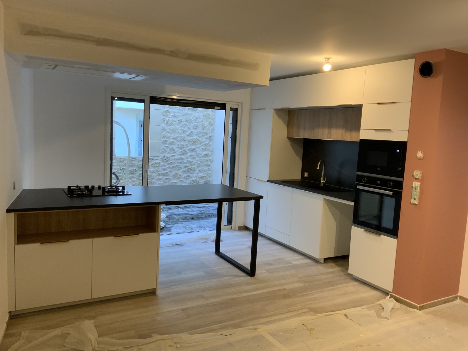 Conception de cuisine blanche mate avec plan snack noir et bloc cuisson en appui mural à Castelnau-le-Lez